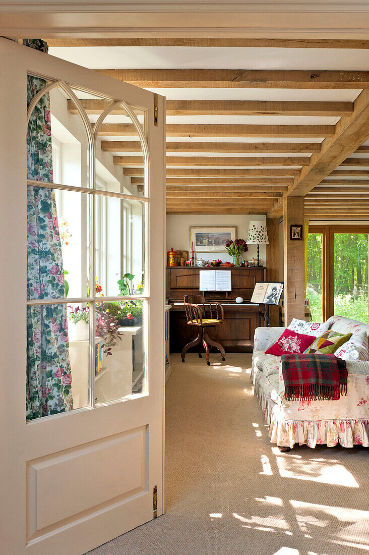 Blick durch die Tür zum Wohnzimmer mit Balkendecke, Sofa und Klavier in einem Haus in Essex, England, UK