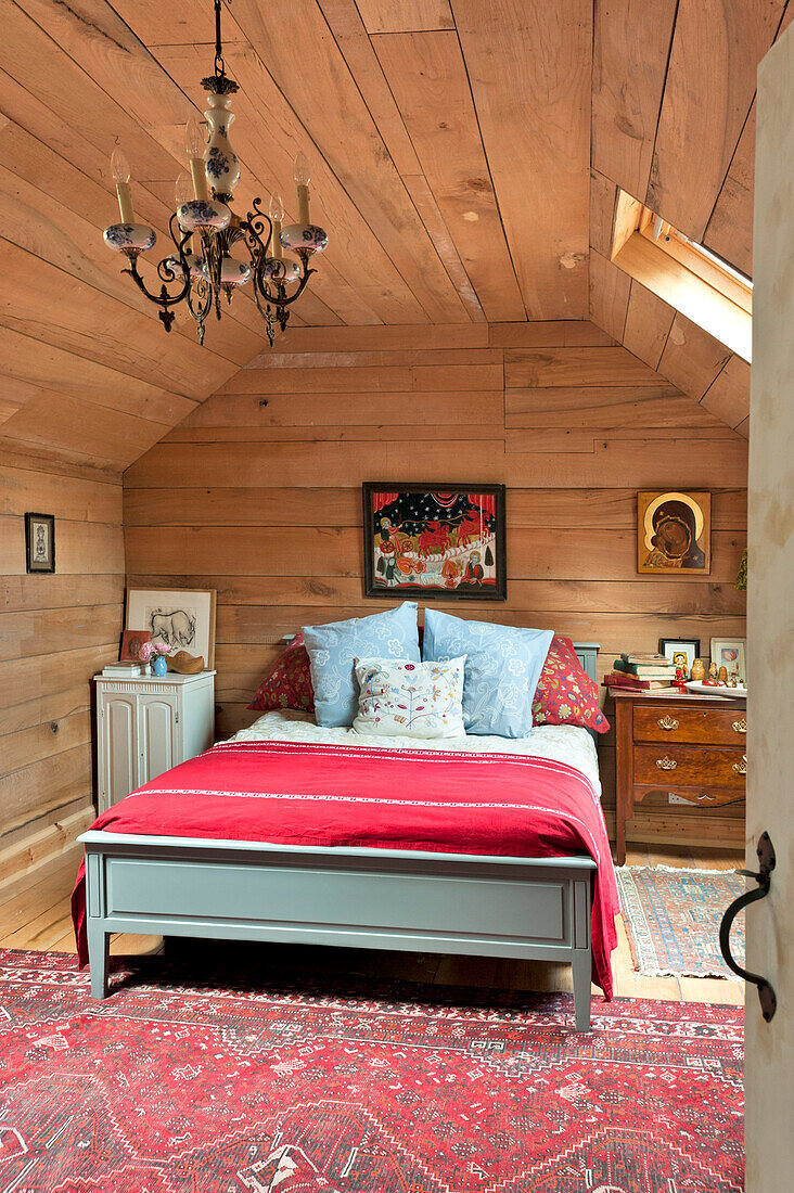 Doppelbett mit roter Decke in einem holzverkleideten Raum mit Vintage-Leuchten, Haus in Essex, England, UK