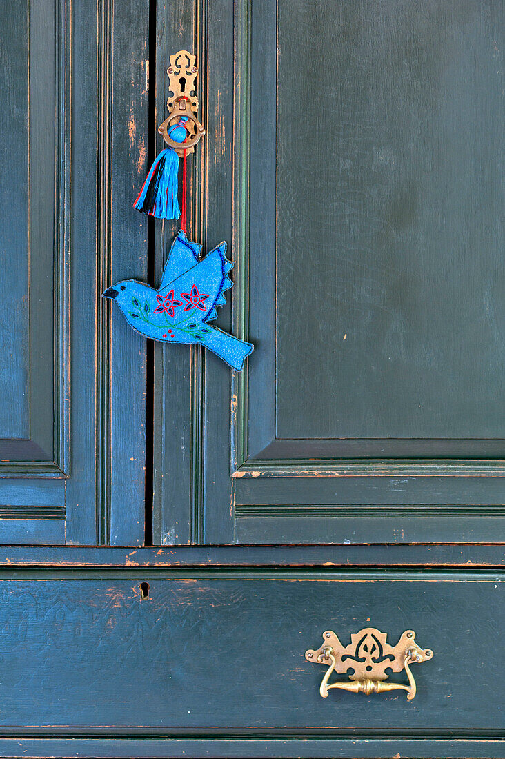 Blue bird hanging on brass handle of painted wardrobe in Essex home, England, UK