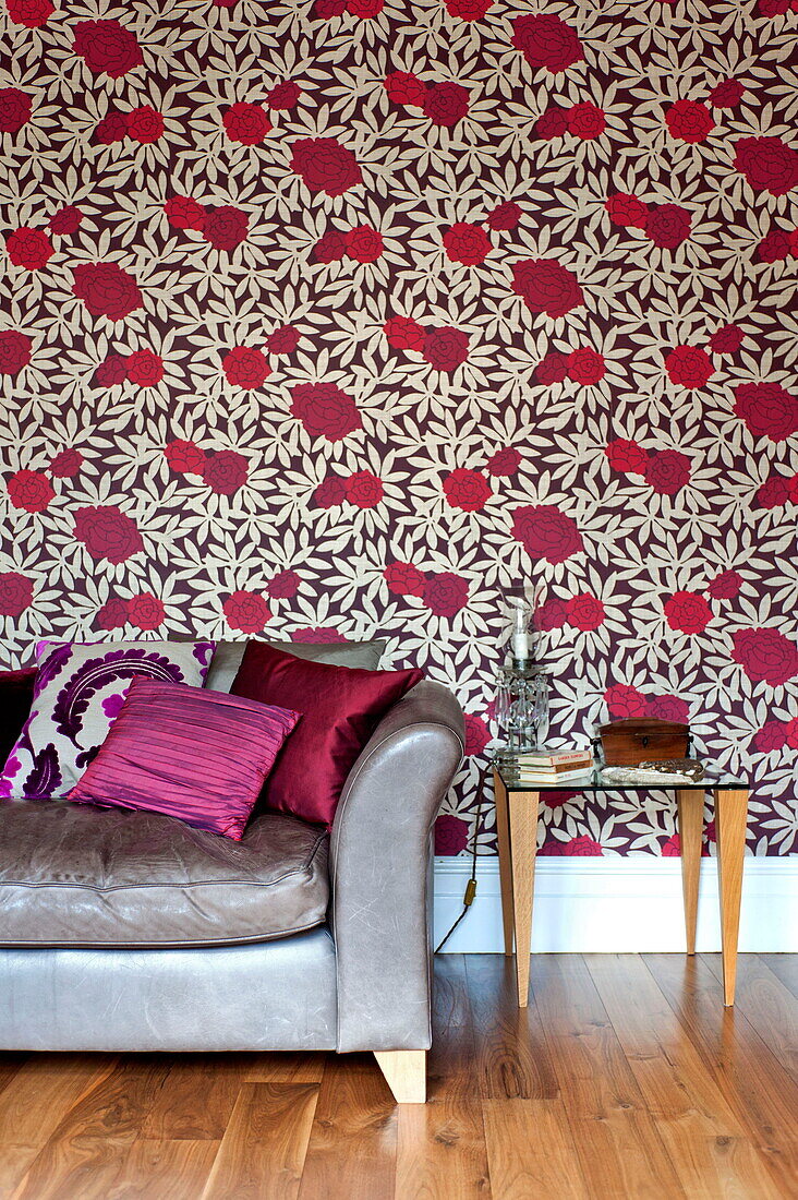 Pink cushions on silver sofa with rose patterned wallpaper in living room of Middlesex family home, London, England, UK