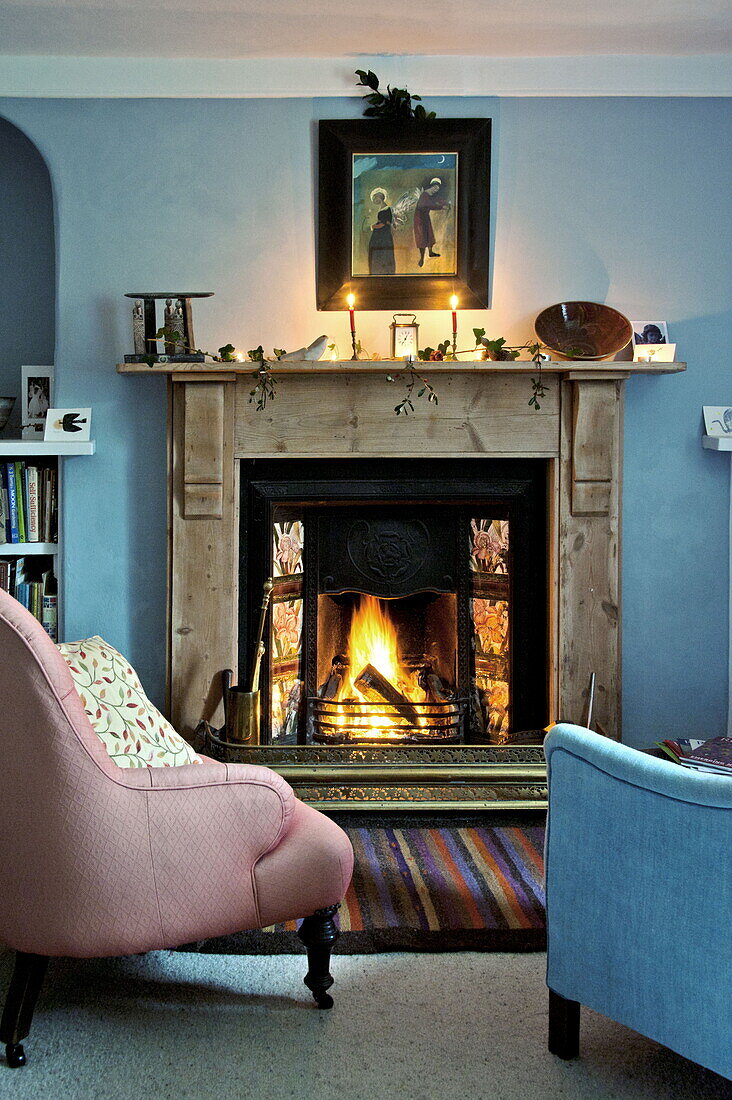 Pink and blue armchairs at fireside of farmhouse, Cornwall, England, UK