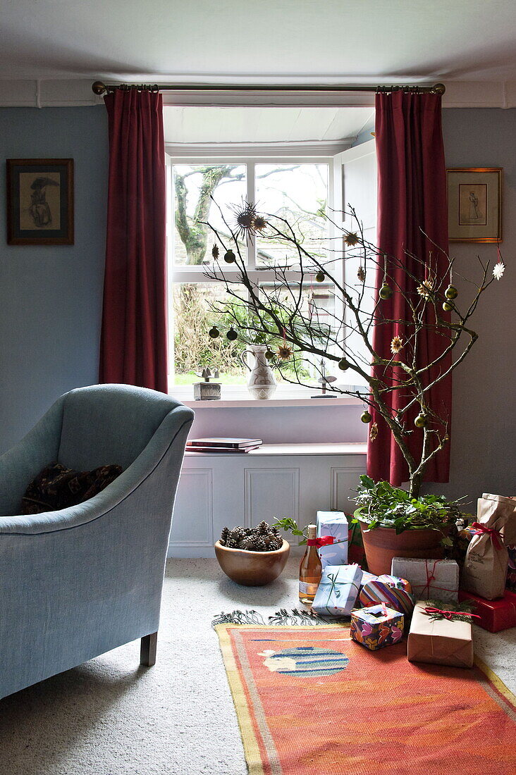 Weihnachtsgeschenke und blauer Sessel im Wohnzimmer eines Bauernhauses, Cornwall, England, Vereinigtes Königreich