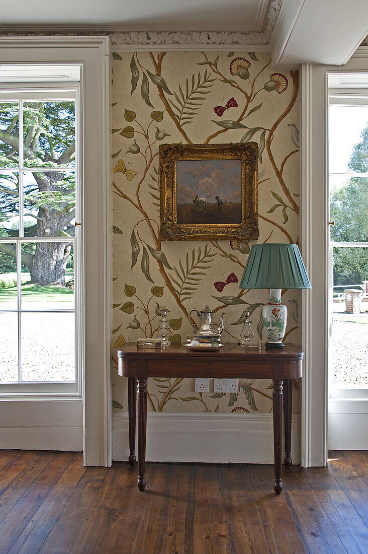 Turquoise lampshade on wooden side table with patterned wallpaper in contemporary Suffolk country house, England, UK