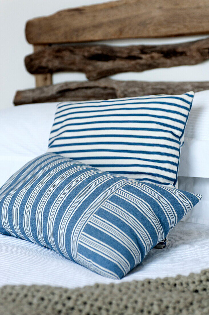 Marine striped cushions on bed with driftwood headboard in Wadebridge home, Cornwall, England, UK