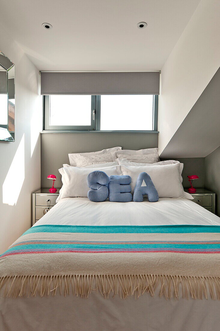 A striped blanket and cushions spelling the word 'SEA' on a double bed under a window in a house in Wadebridge, Cornwall, England, UK