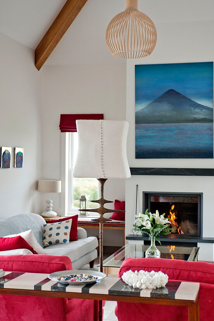 Standard lamp and artwork wit lit fire in living room of contemporary home, Cornwall, England, UK