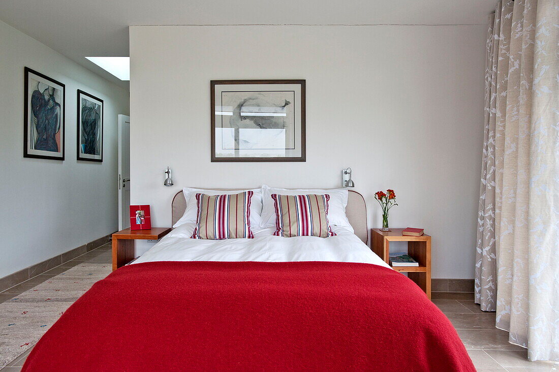 Rote Wolldecke auf einem Doppelbett mit gestreiften Kissen in einem modernen Haus, Cornwall, England, UK