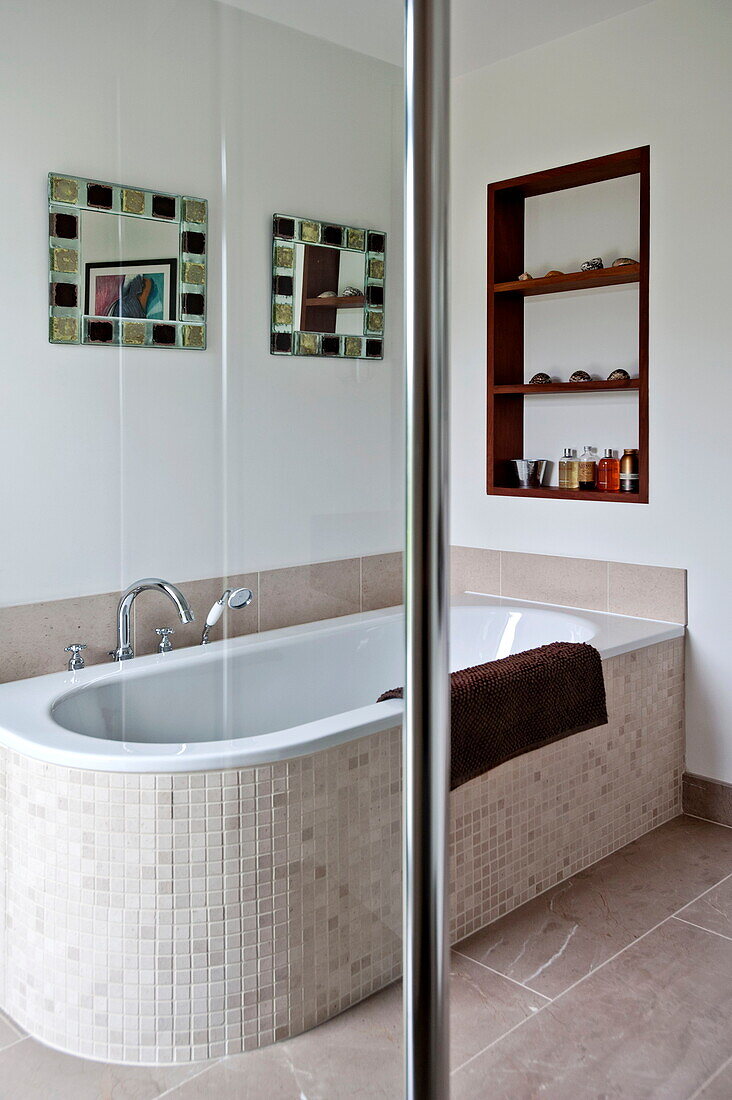 Mosaikgefliestes Bad mit eingelassenen Regalen und Spiegel in einem modernen Haus, Cornwall, England, UK
