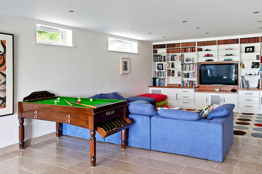 Blaues Sofa und Billardtisch mit Fernseher und Regalen im Spielzimmer eines modernen Hauses, Cornwall, England, UK