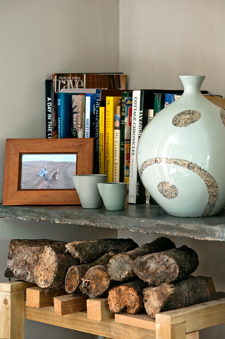 Vase and books on shelf above firewood in Padstow cottage, Cornwall, England, UK