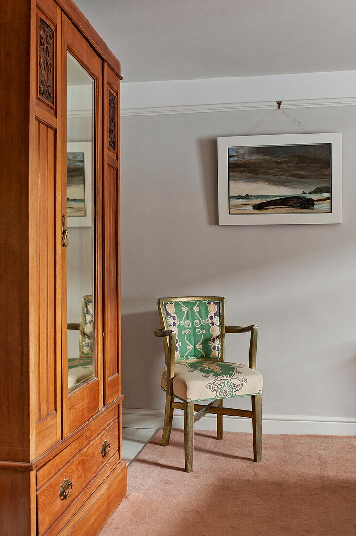 Antique wooden wardrobe and artwork with chair in bedroom of Padstow cottage, Cornwall, England, UK