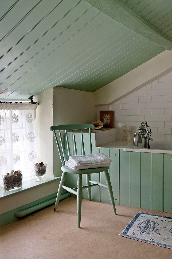 Gefaltete Handtücher auf einem Stuhl in einem grün gestrichenen Badezimmer im Dachgeschoss eines Cottage in Padstow, Cornwall, England, UK