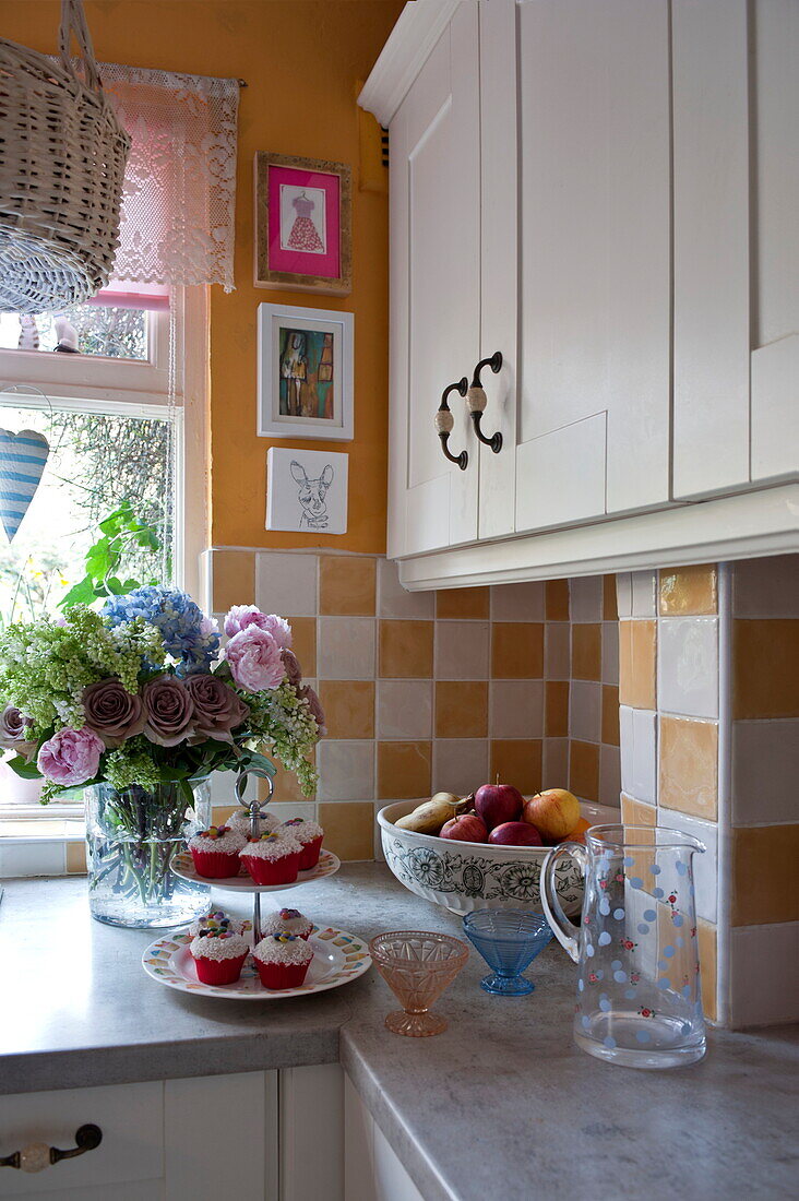 Cupcakes auf Arbeitsplatte in Küche mit weißen Einbaugeräten und karierter Spritzschutzwand, London, England, Vereinigtes Königreich