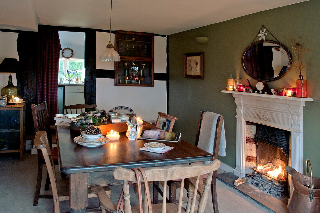 Wooden dining table and chairs with lit fire in Shropshire cottage, England, UK