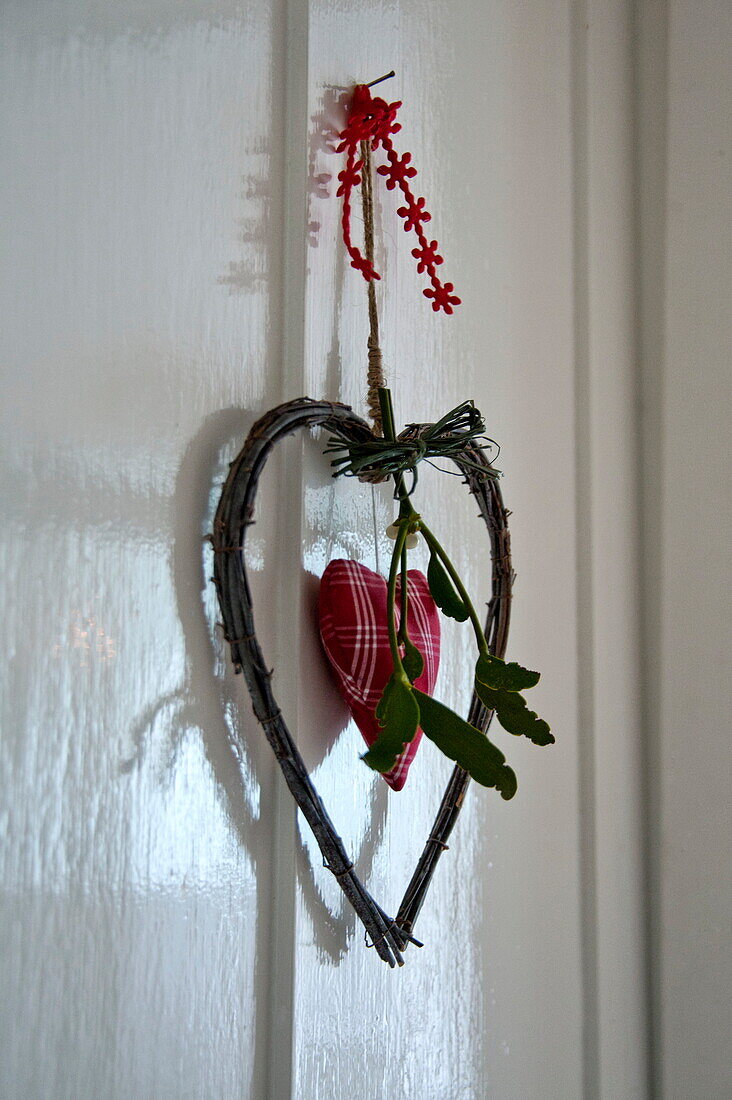 Herzförmiges Ornament mit Mistelzweig an weiß getäfelter Tür in einem Cottage in Shropshire, England, Vereinigtes Königreich