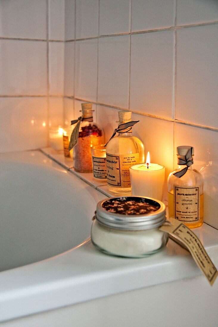 Lit candles and bath oils in tiled white bathroom of Shropshire cottage, England, UK