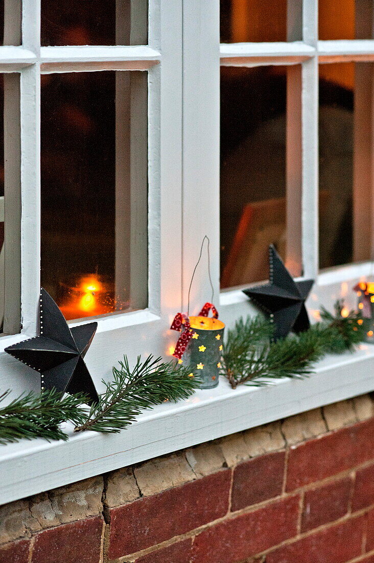 Beleuchtete Kerzen und Weihnachtsdekoration auf der Fensterbank eines Cottage in Shropshire, England, UK