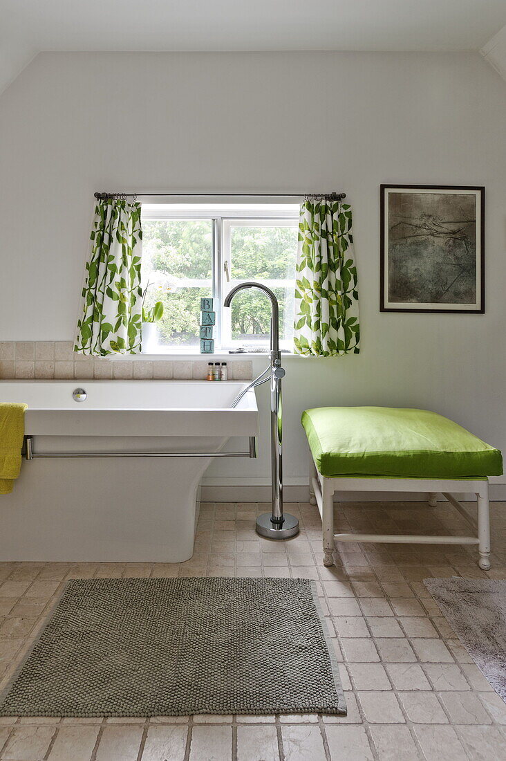 Blattgemusterte Vorhänge am Fenster im Badezimmer mit lindgrünem Sitzbezug in einem modernen Haus in Suffolk/Essex, England, UK