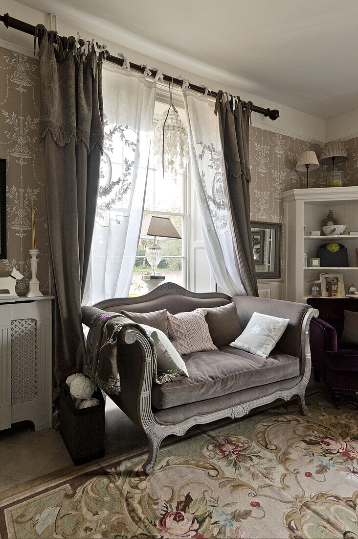 Bestickte Gardinen über einem zweisitzigen Sofa aus braunem Samt im Wohnzimmer eines Landhauses in Bury St Edmunds, Suffolk, England, UK