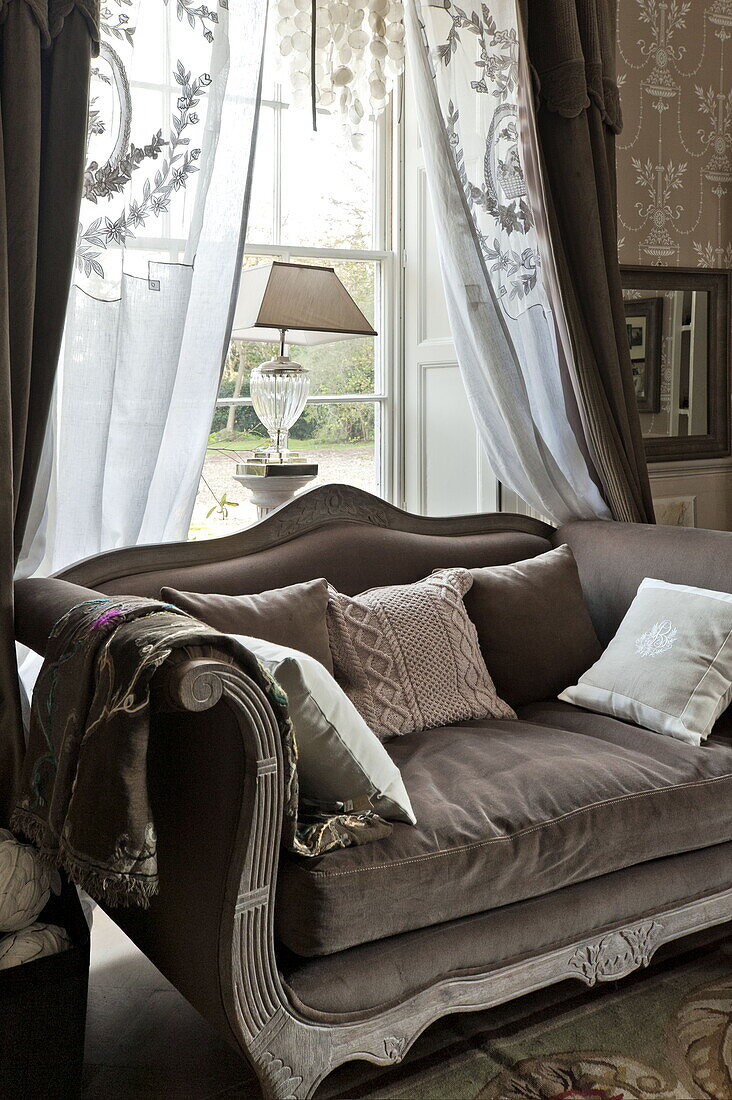 Bestickte Gardinen über einem zweisitzigen Sofa aus braunem Samt im Wohnzimmer eines Landhauses in Bury St Edmunds, Suffolk, England, UK