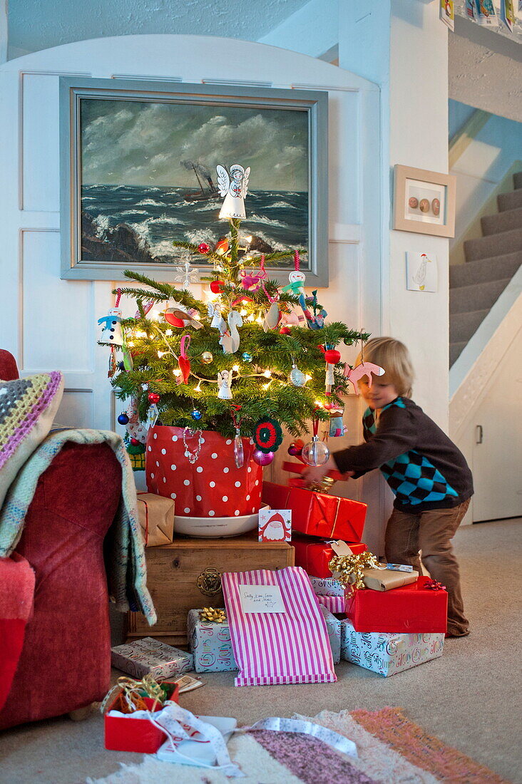 Young boy looking at presents under Christmas tree in Penzance home Cornwall England UK