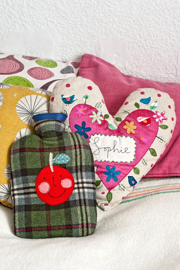 "Herzförmiges Kissen mit dem Wort Sophie"" und einer Wärmflasche auf dem Bett in einem Cottage in Penzance, Cornwall, England UK"""