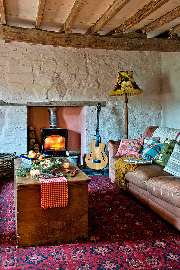 Sofa and wooden chest with patterned rug and lit wood burning stove in living room of Tregaron home Wales UK