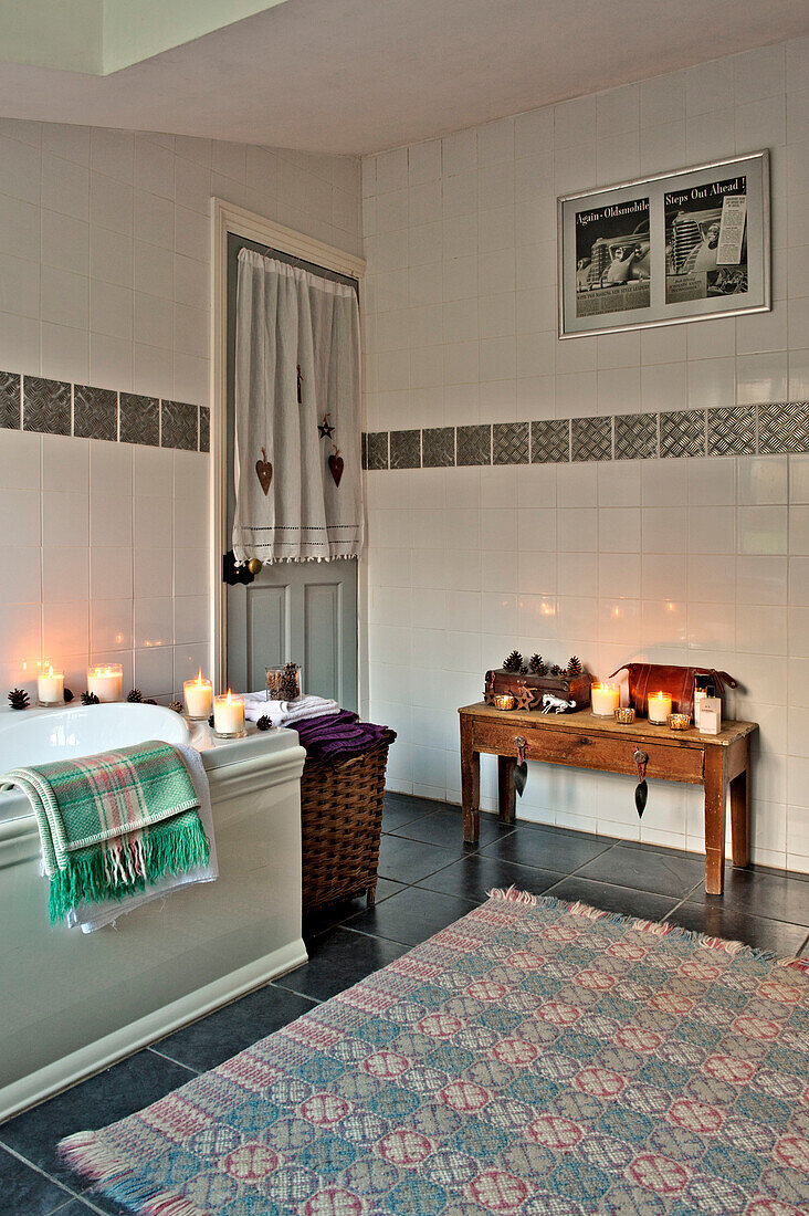Kerzenlicht und Badewanne mit hölzernem Beistelltisch und gemustertem Teppich im Badezimmer eines Hauses in Tregaron, Wales, UK