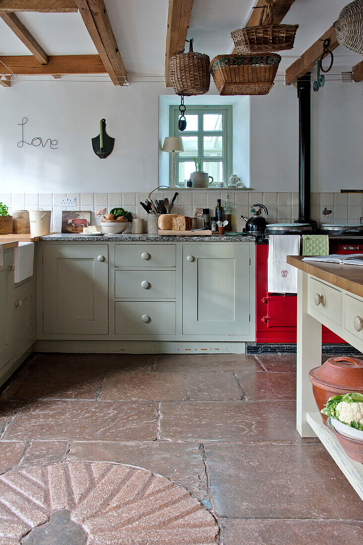 Körbe hängen in der Balkendecke einer Bauernhausküche mit Fliesenboden in einer umgebauten Scheune in Sherford, Devon, Großbritannien