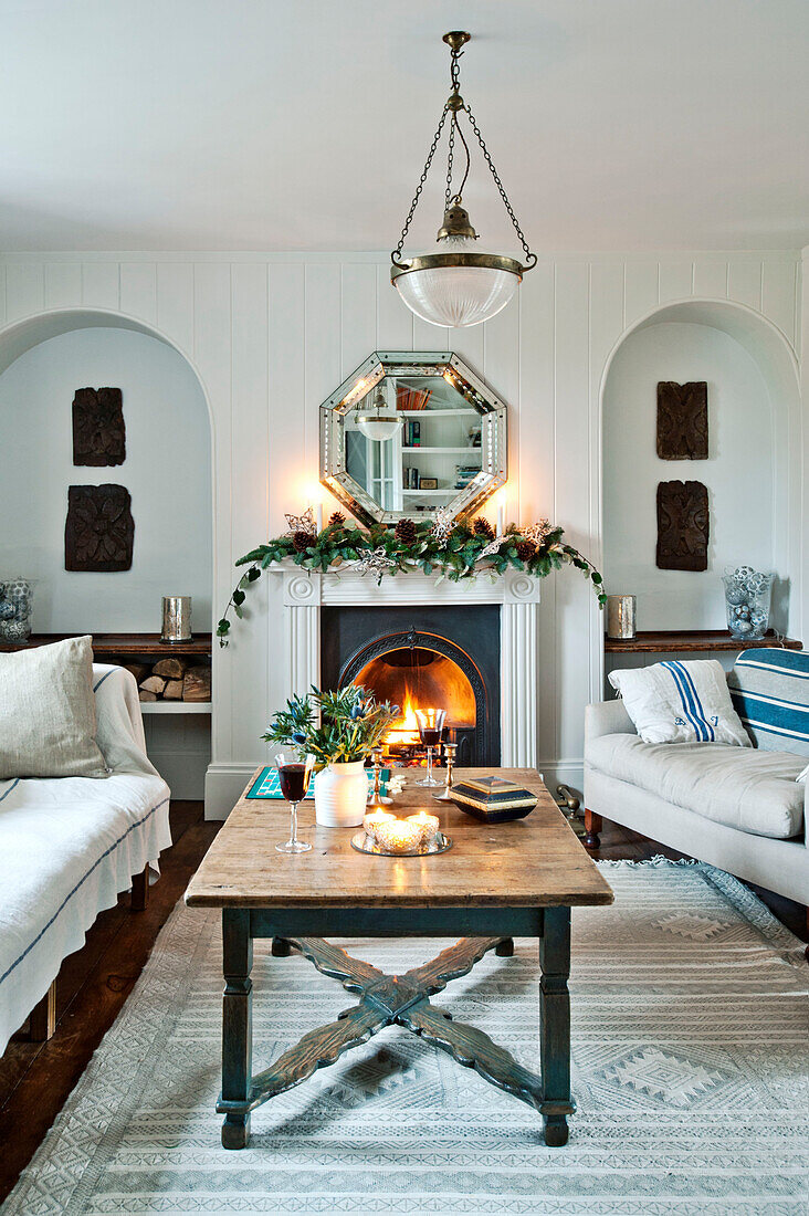 Octagonal mirror above lit fire with wooden coffee table in Crantock home Cornwall England UK