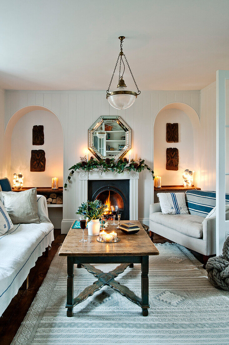 Octagonal mirror above lit fire with wooden coffee table in Crantock home Cornwall England UK