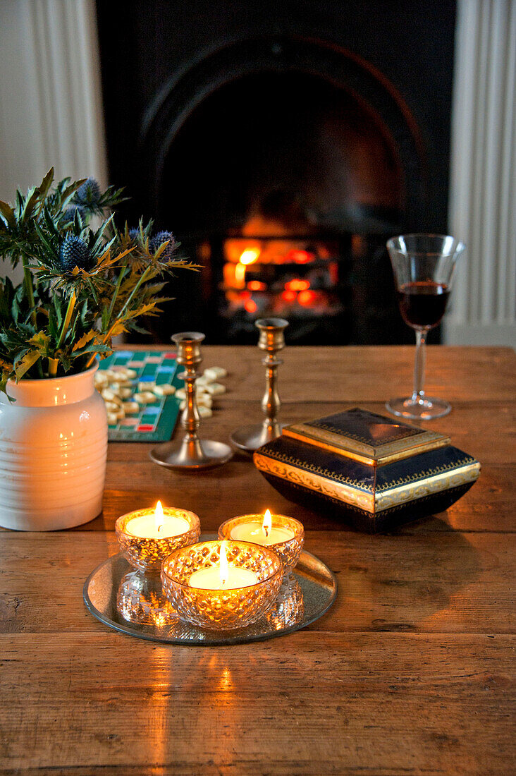 Angezündete Kerzen mit geschnittenen Disteln auf dem Tisch am Feuer mit Glut in Crantock home Cornwall England UK