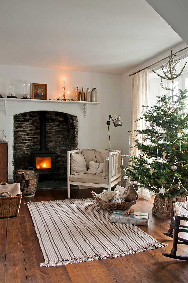 Weihnachtsbaum und Sessel mit Holzofen in einem Haus in Crantock, Cornwall, England UK