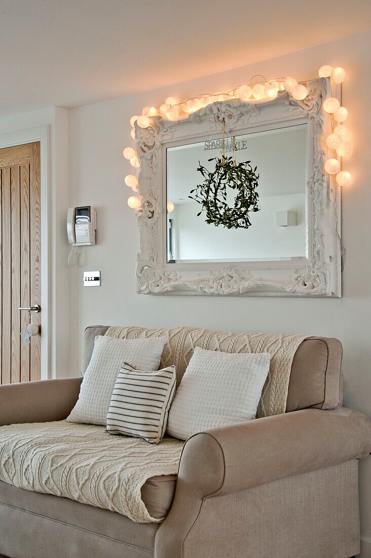 Beleuchtete Lichter auf dem Spiegel über dem Zweisitzer-Sofa mit Mistelzweig, Haus in Wadebridge, North Cornwall, UK
