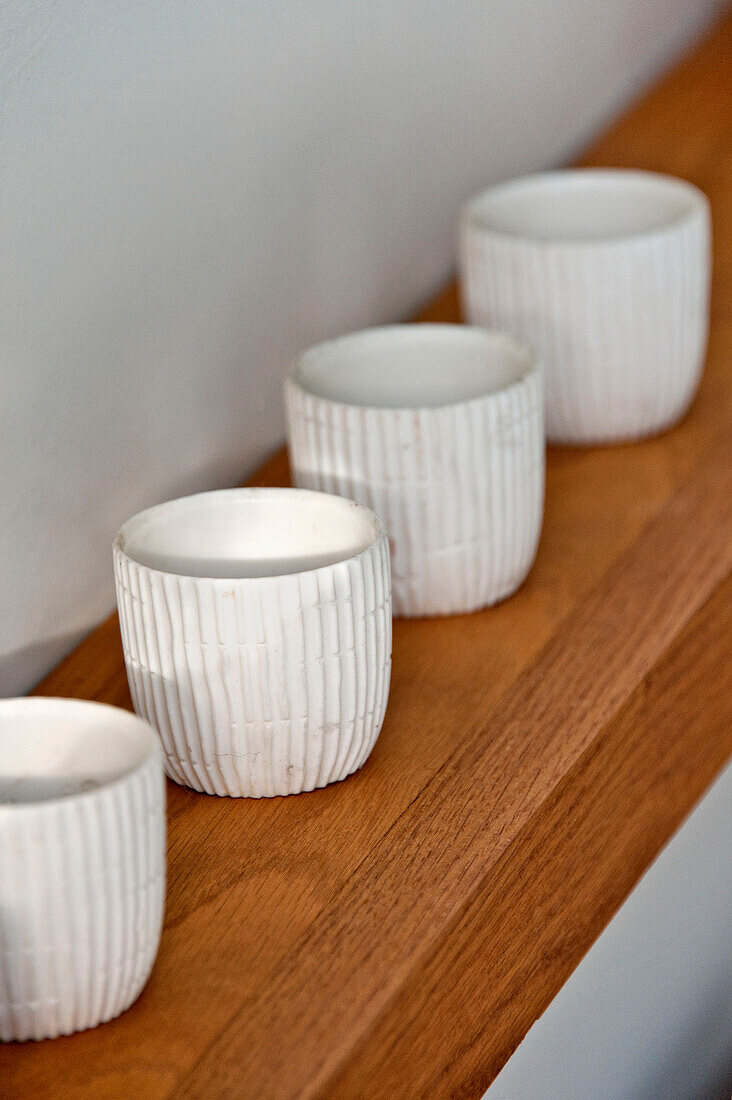 Simple white tealight holders on wooden shelf in Cornwall home, UK