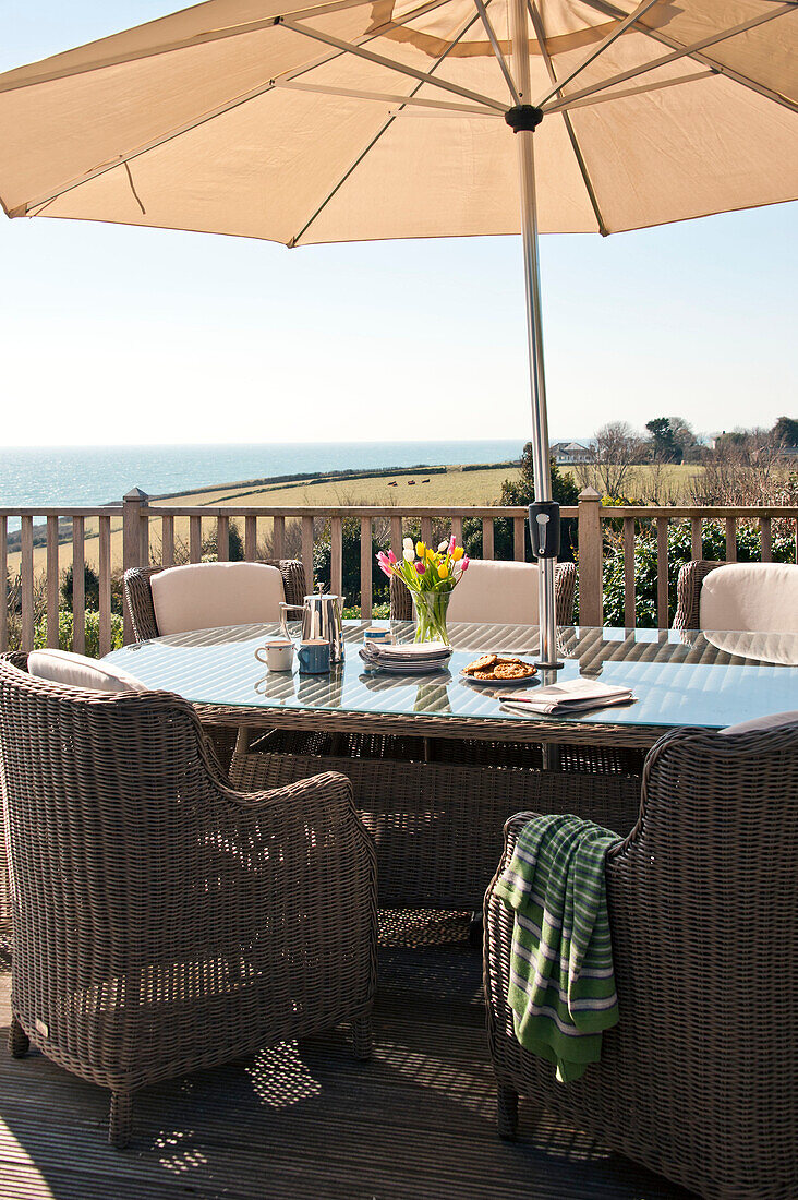 Wicker chairs at table with parasol on terrace, Cornwall, UK