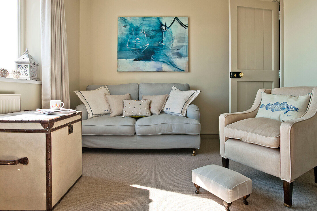 Cream armchair with light grey sofa and modern artwork in living room of family home Cornwall UK