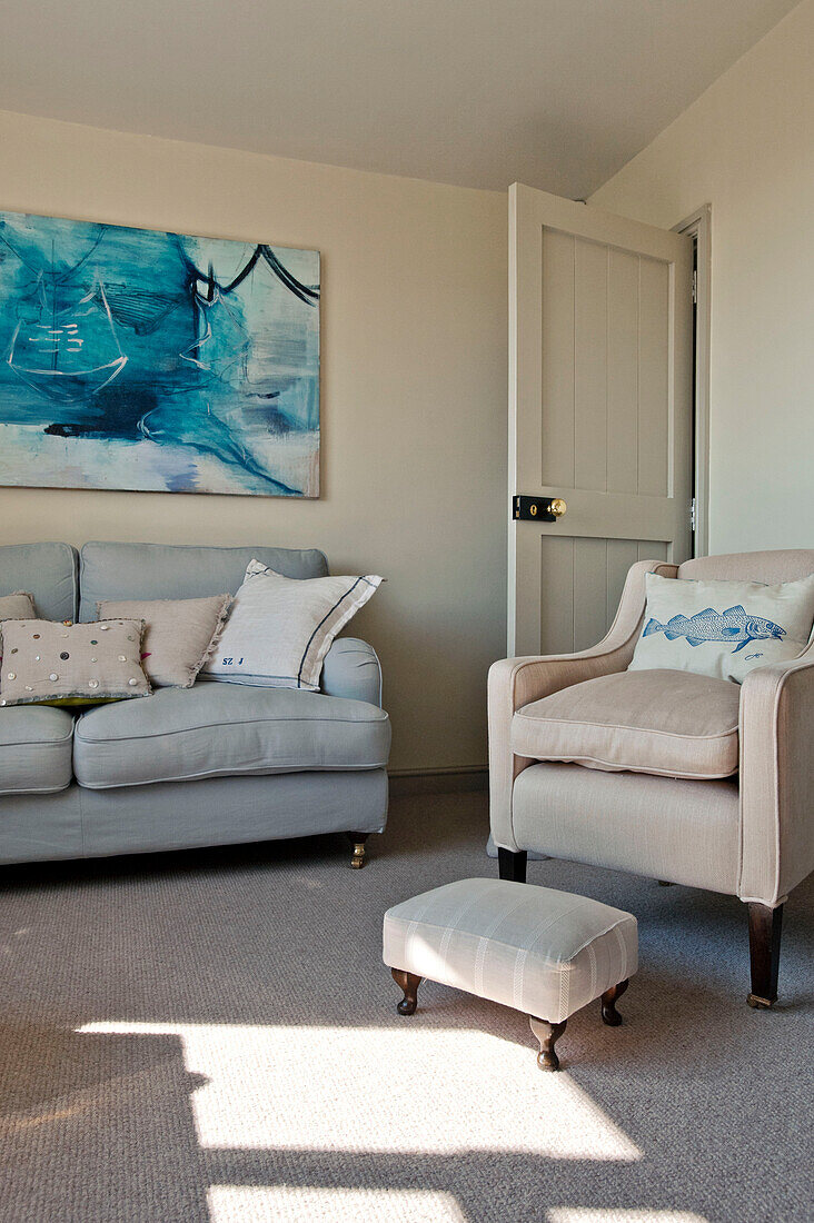 Cream armchair and footstool with light grey sofa and modern artwork in living room of family home Cornwall UK