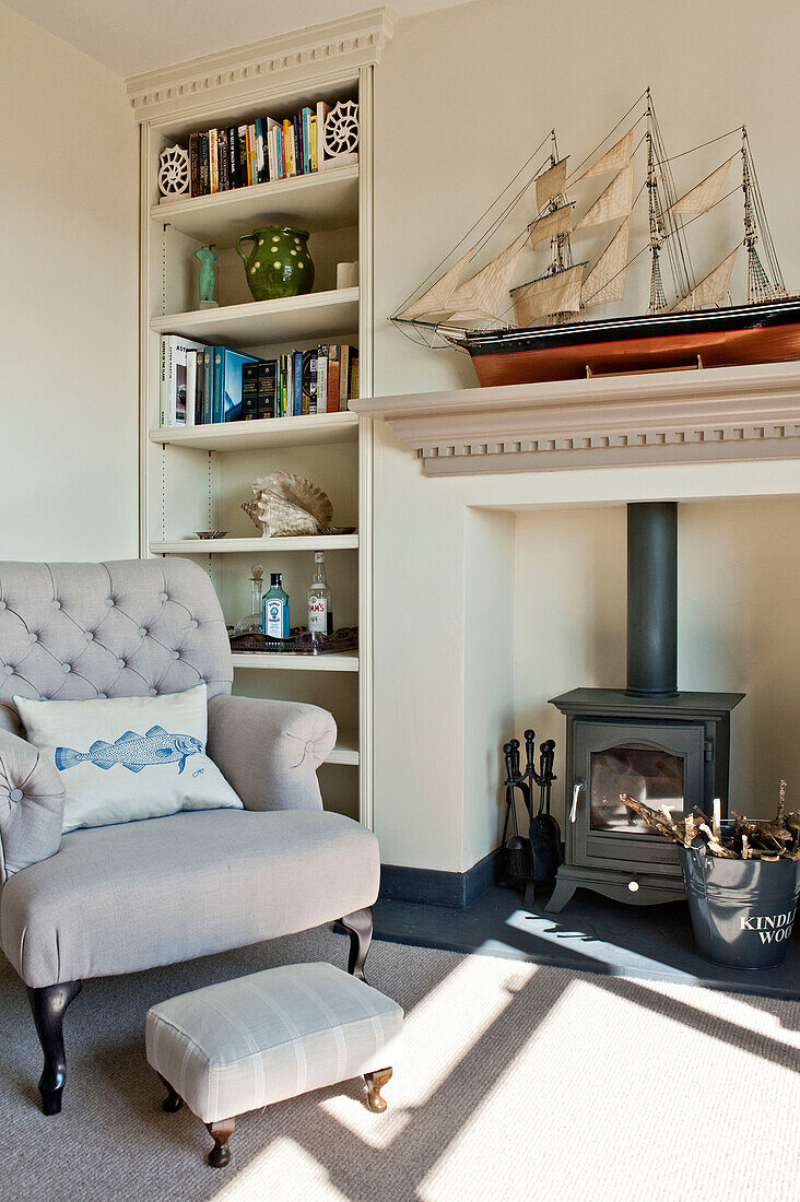 Sessel und Fußhocker am Kamin mit Schiffsmodell auf dem Kaminsims im Wohnzimmer eines Familienhauses Cornwall UK