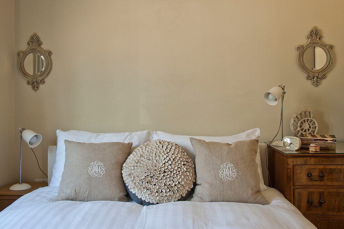 Square and circular linen cushions on double bed in family home, Cornwall, UK