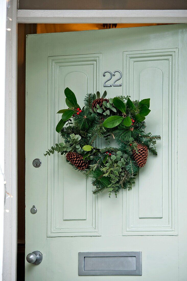 Floraler Weihnachtskranz an pastellgrüner Eingangstür in einem Haus in Penzance, England UK