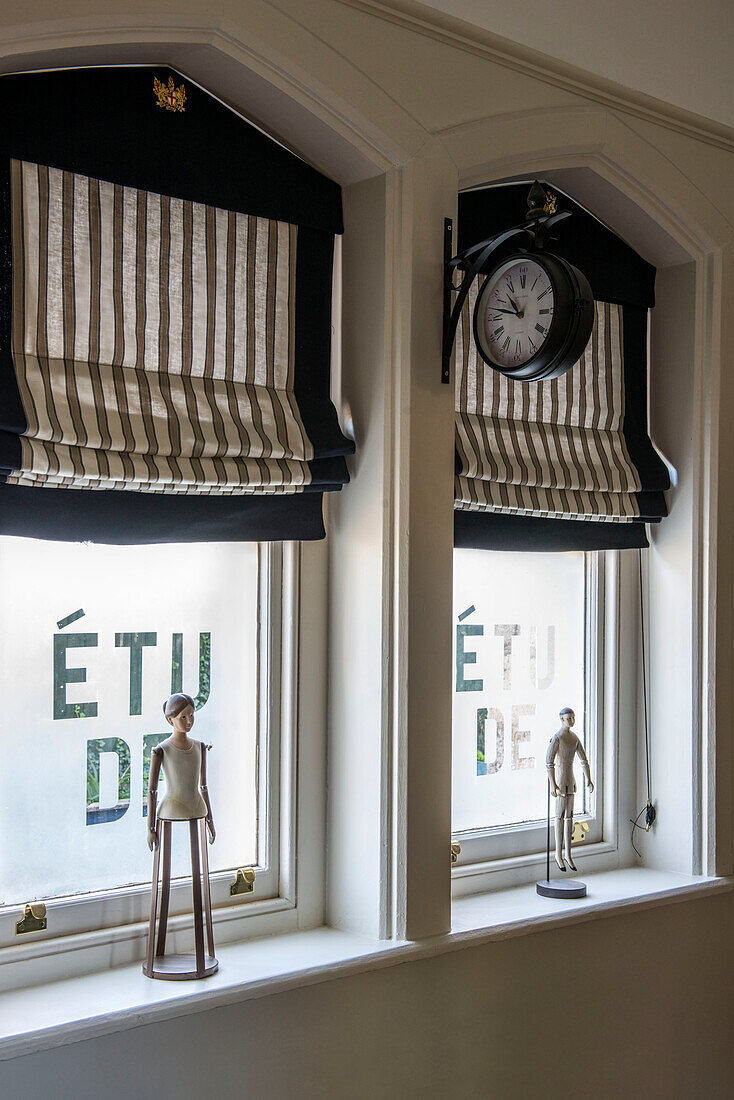 Figurines and French text with Roman blinds and clock in windows of Stamford home Lincolnshire England UK