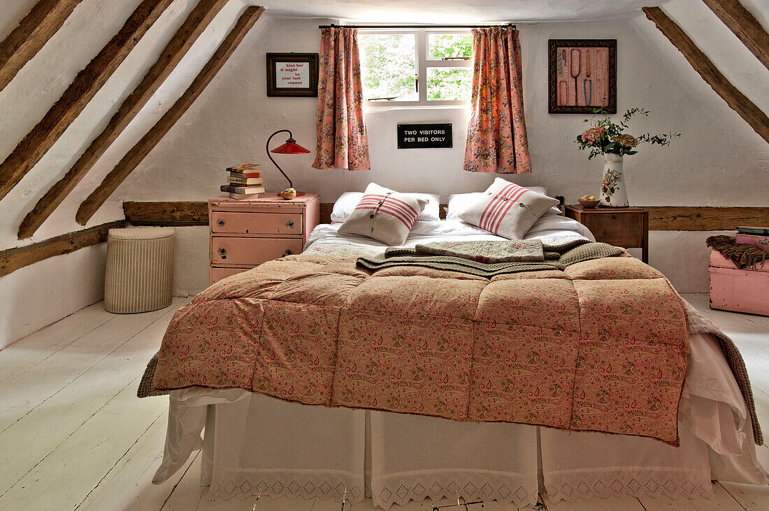 Double bed at window in timber framed attic bedroom of Cambridge cottage England UK