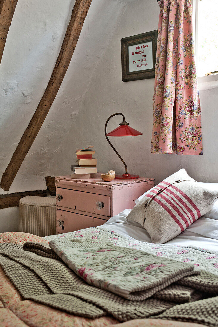 Rote Vintage-Lampe auf rosafarbenem Nachttisch mit geblümten Vorhängen in einem Cottage mit Holzrahmen in Cambridge (England)