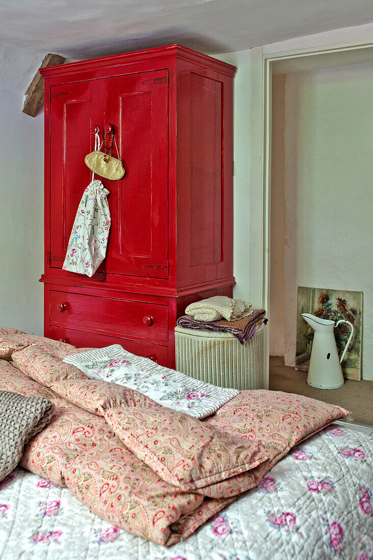 Red painted wardrobe in bedroom with floral quilts in Cambridge cottage England UK