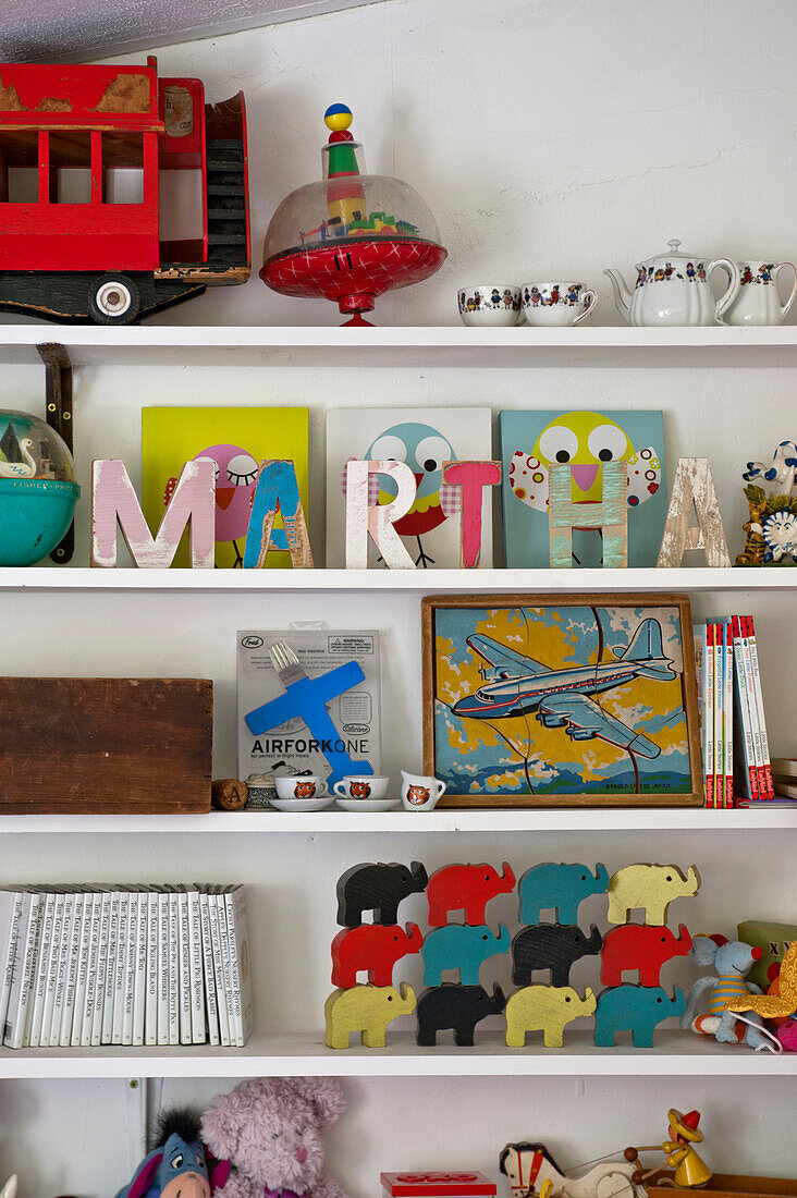 Spielzeug und Kunstwerke mit dem Namen 'MARTHA' auf Regalen im Mädchenzimmer eines Cottage in Cambridge, England UK