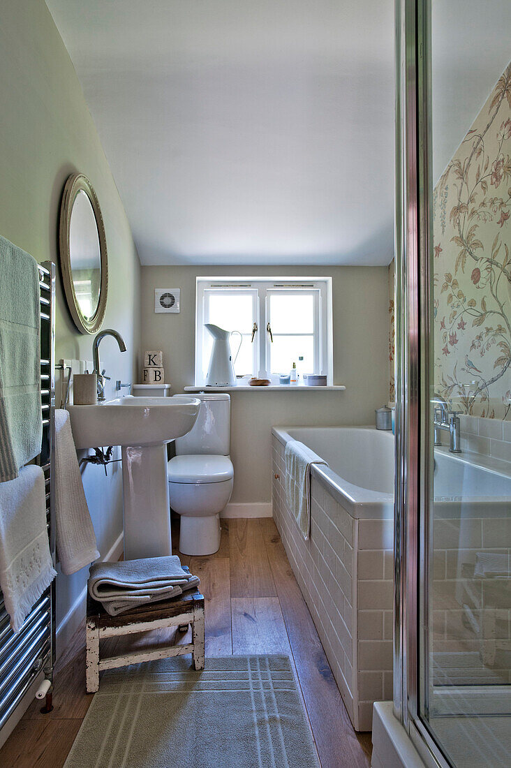 Runder Spiegel über Sockelbecken mit niedrigem Hocker in Cambridge cottage bathroom England UK