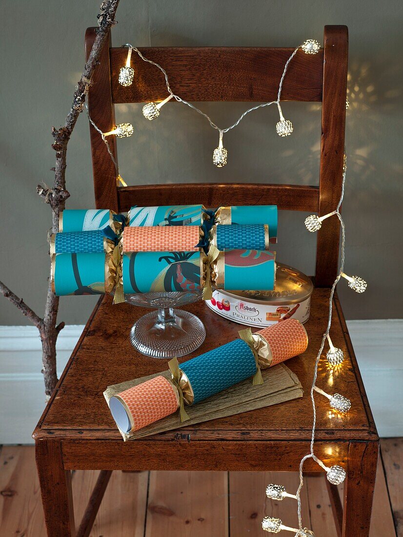Lit fairylights and Christmas crackers on wooden chair in London home England UK