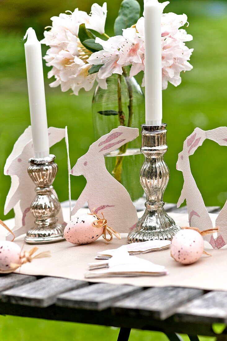 Osterhasen und silberne Kerzenständer mit Schnittblumen auf dem Gartentisch in Sussex England UK
