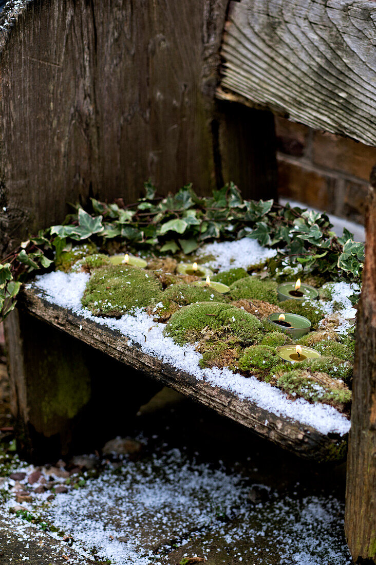 Lit tealights and moss-covered wooden bench seat in London garden England UK